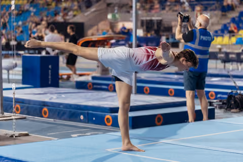 Young gymnast holds a precise arabesque on the floor, focused and controlled, at an indoor gymnastics competition.