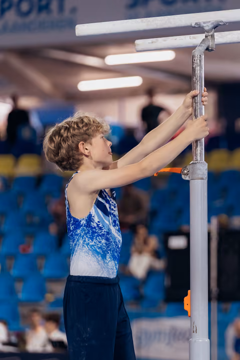 Focused young male gymnast in blue leotard carefully adjusts the horizontal bar height before his routine.