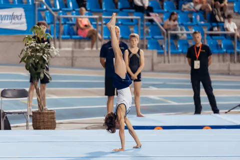 Young gymnast performs a one-handed cartwheel on the floor mat during a competition, legs split high in the air.