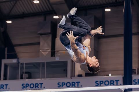 Male gymnast mid-flight, body fully inverted above the parallel bars, arms outstretched, intense focus during competition.