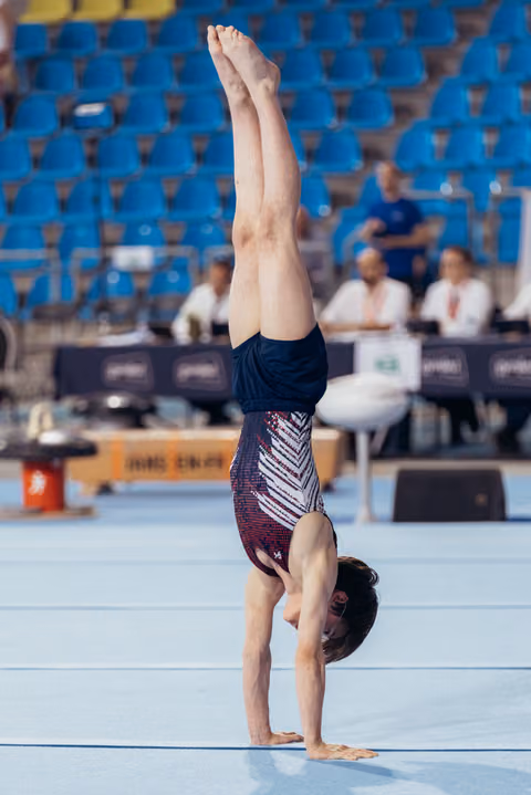 Young male gymnast performs a perfect handstand on the floor exercise mat during a competition, legs straight overhead.