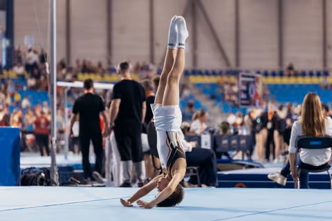 Gymnast performs a precise handstand on the floor exercise mat during a competitive gymnastics event, legs perfectly vertical.