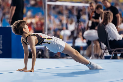 Young male gymnast holds a push-up position on the blue floor mat during a gymnastics event, focused and composed.