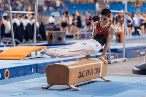 Young male gymnast holds a planche position on a pommel horse, body parallel to the floor, intense concentration.