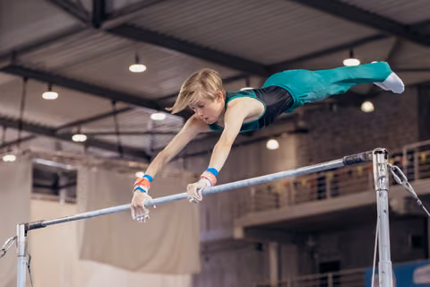 Young male gymnast performs a horizontal bar routine, body fully extended parallel to bar, intense focus, indoor gym.