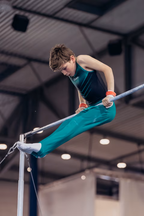 Young male gymnast concentrating intensely on parallel bars, body leaning forward with controlled strength in an indoor gym.