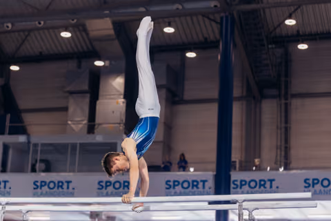 Young male gymnast performs a perfect handstand on parallel bars, body fully extended, at Sport Vlaanderen competition hall.