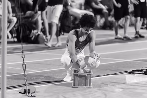 Young gymnast crouches intently over a chalk box on an indoor athletics track, preparing for a routine.
