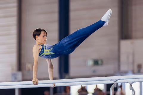 Focused young male gymnast performing a straight horizontal hold on parallel bars, legs extended, wearing blue and yellow leo.