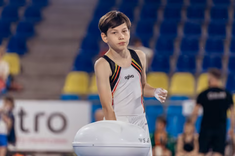 Young male gymnast chalking hands before vault attempt, looking focused and composed in a competitive arena.