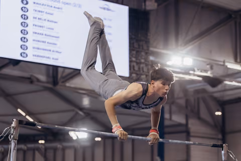 Young male gymnast performs a horizontal bar routine, body parallel to the bar, intense focus, at an indoor competition.
