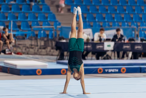 Young gymnast performs a perfect handstand on floor exercise, legs stretched upward, wearing a green leotard at a competition.