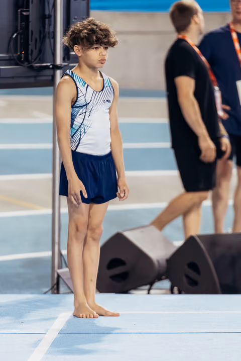 Young male gymnast stands barefoot on the floor exercise mat, looking focused and composed before his routine.