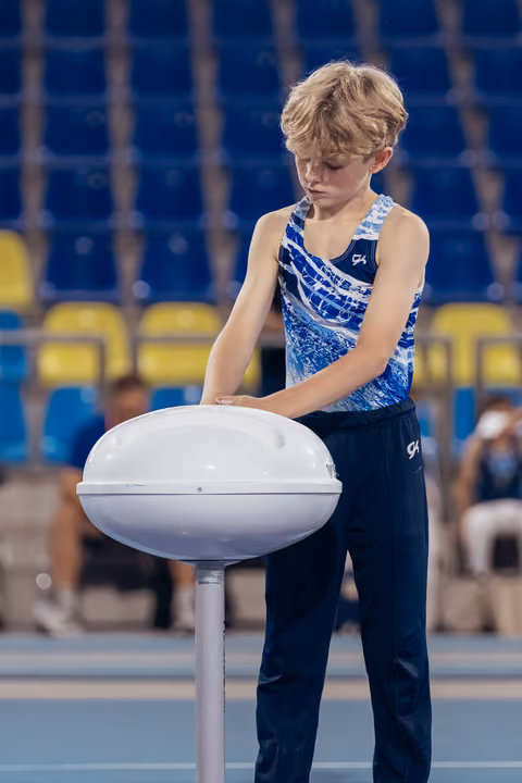Young male gymnast chalking his hands at a chalk bowl, focused and composed before his routine in an arena.