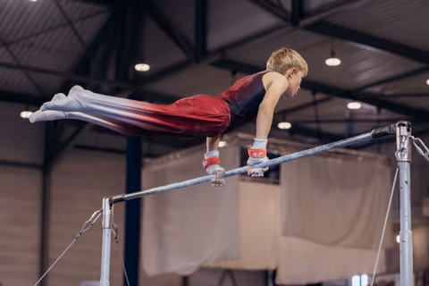 Young male gymnast holds a front lever on the horizontal bar, body fully extended, intense focus in an indoor gymnastics hall.