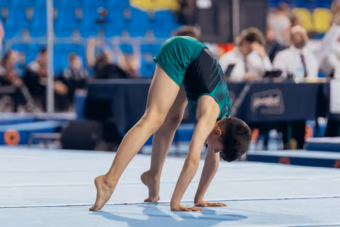 Young male gymnast bent in deep pike position on floor mat, focused and controlled, during competition.