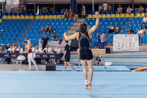 Male gymnast raises fist in triumph after landing on floor exercise mat during indoor gymnastics competition.