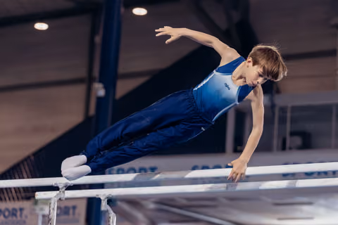 Young male gymnast performs a powerful hold on parallel bars, body extended horizontally, focused expression in indoor gym.