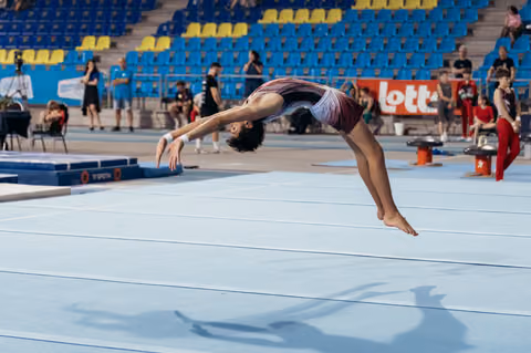 Young gymnast performs a powerful backflip on the floor exercise mat, body arched gracefully mid-air during competition.
