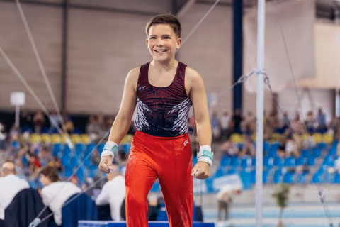 Young male gymnast celebrates with fists clenched and a beaming smile after his routine in a packed arena.
