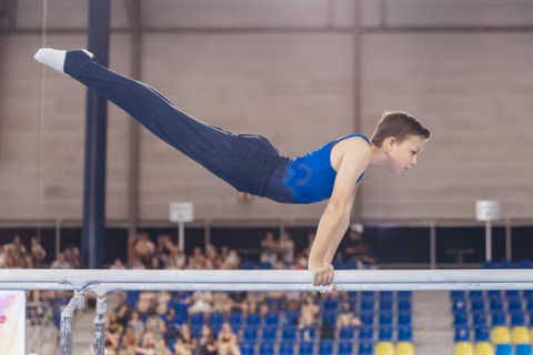 Young male gymnast holds a perfect planche on parallel bars, body fully horizontal, expression intense with concentration.