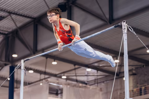 Young boy with glasses performs a dynamic release on the horizontal bar, showing intense focus and precision indoors.