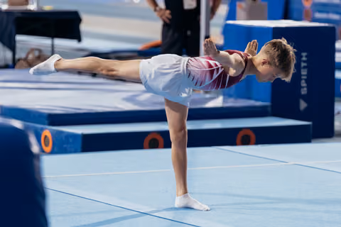 Young gymnast performs a precise arabesque on the floor, showing strong focus and body control at a gymnastics meet.