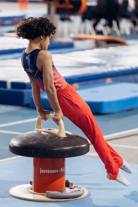 Young male gymnast holds a difficult position on the pommel horse, body horizontal, showing strength and concentration.