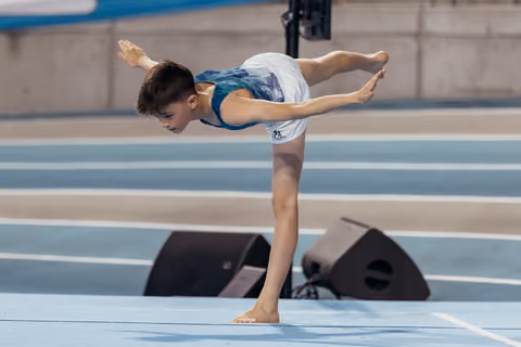 Young male gymnast performs a focused arabesque balance on the floor exercise mat during a competition.