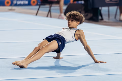 Young male gymnast holds a side support pose on the floor mat, focused and determined during a gymnastics event.