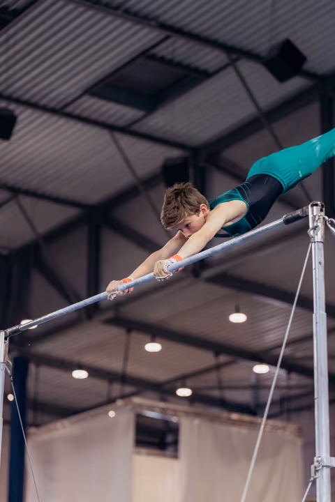 Young male gymnast grips the horizontal bar with fierce concentration, body stretched horizontal in a gymnastics hall.