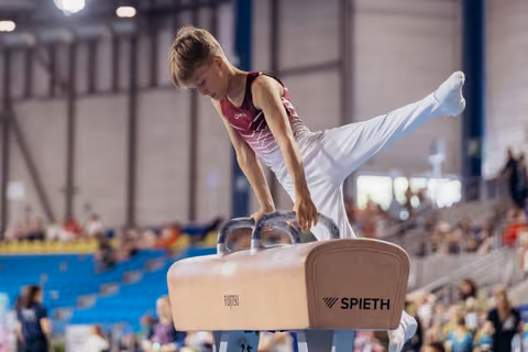 Young male gymnast concentrating intently while performing on the pommel horse at an indoor gymnastics meet.