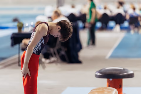 Young male gymnast bows toward pommel horse, showing concentration and determination before his routine at an indoor meet.