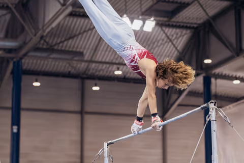 Young male gymnast performs an inverted release on the high bar, body arched with fierce concentration in an indoor gym.