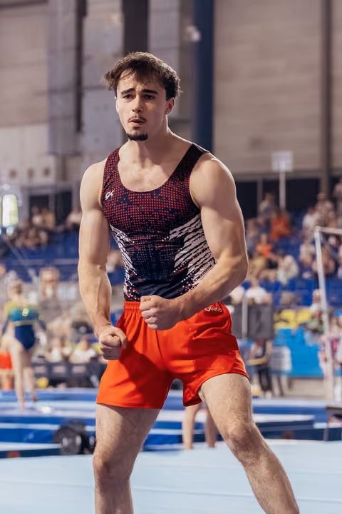 Young male gymnast celebrates with clenched fists, showing determination and intensity on the competition floor.