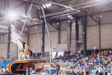 Male gymnast performs an inverted handstand on a Spieth vault during a packed indoor gymnastics competition.