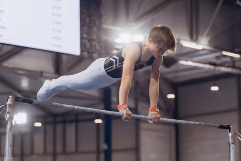 Young male gymnast holds a planche on the horizontal bar, body fully extended, intense focus on his face, indoor arena.