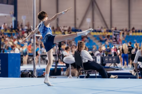 Young gymnast performs a precise arabesque on the floor exercise, arms outstretched, showing poise and concentration at a competition.