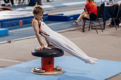Young male gymnast concentrating intensely while performing a support hold on a mushroom apparatus during a competition.