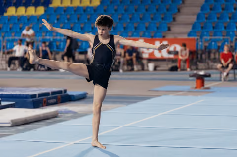 Young male gymnast performs a focused arabesque balance on the floor exercise mat during a gymnastics competition.