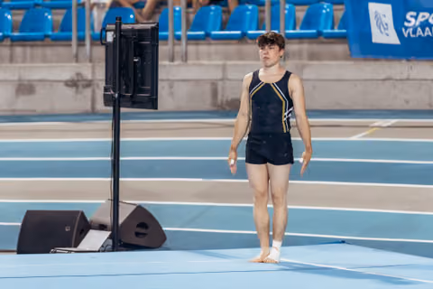Young male gymnast stands barefoot on the floor exercise mat, composed and focused, preparing for his routine.