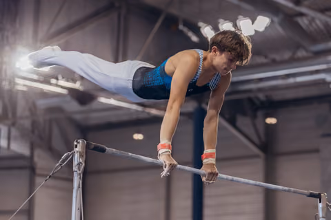 Young male gymnast performs a horizontal bar routine, body horizontal, intense focus, in an indoor sports hall.