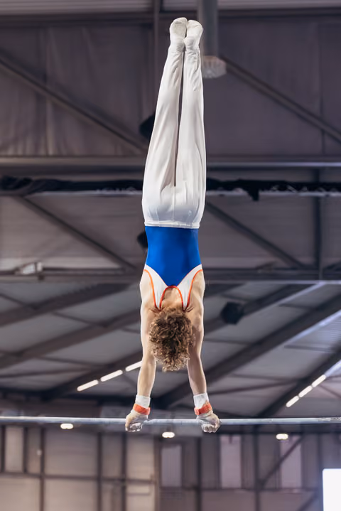 Young male gymnast performs a perfect handstand on horizontal bar, body fully extended, in indoor gymnasium.