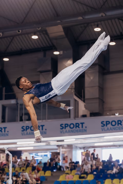 Male gymnast executes a powerful horizontal hold on parallel bars, body fully extended, expression intense, at Sport Vlaanderen event.