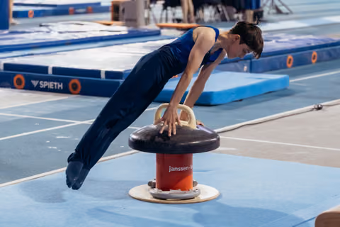 Young male gymnast performs a planche hold on a mushroom apparatus, body perfectly horizontal, focused expression, indoor gym.
