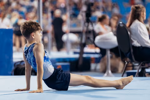 Young male gymnast performs a cobra stretch on the floor mat, focused and composed during a gymnastics meet.