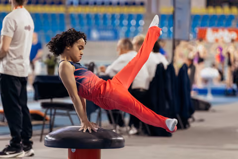 Young gymnast performs a focused straddle hold on a mushroom apparatus during a gymnastics event.