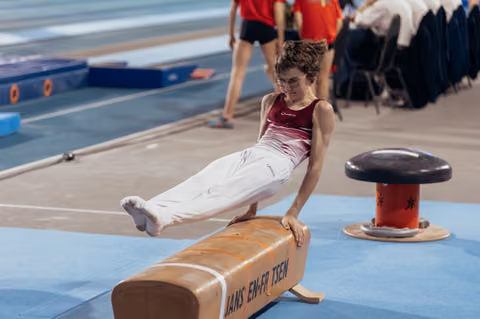 Young gymnast with glasses performs a straddle hold on the pommel horse, concentrating intensely during competition.