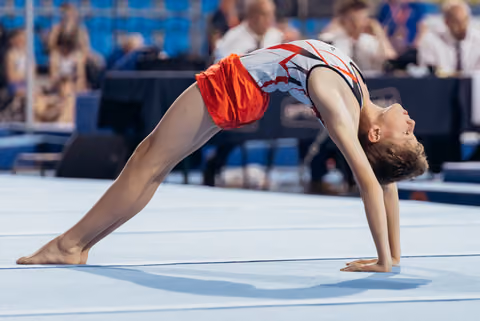 Young gymnast performs a deep backbend on the floor mat, head tilted back with concentration during a competition.