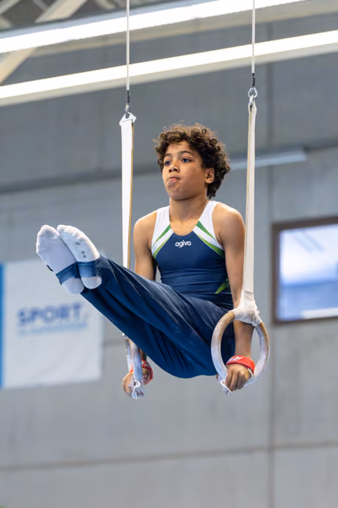Young athlete performing a horizontal hold on still rings, displaying focused determination during training at an indoor facility